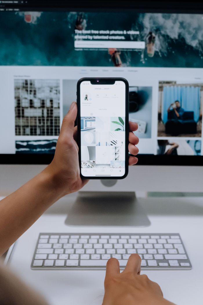 About Person uses a smartphone in front of a computer screen displaying stock photos, showcasing modern technology use.